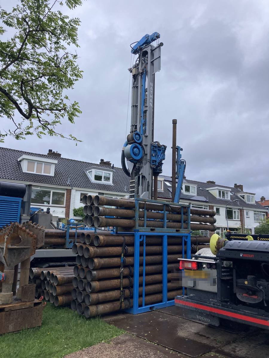 Boorinstallatie voor de proefboring in het Ramplaankwartier: een hoge mobiele boortoren met stapels boorbuizen, opgesteld op straat tussen de rijwoningen.