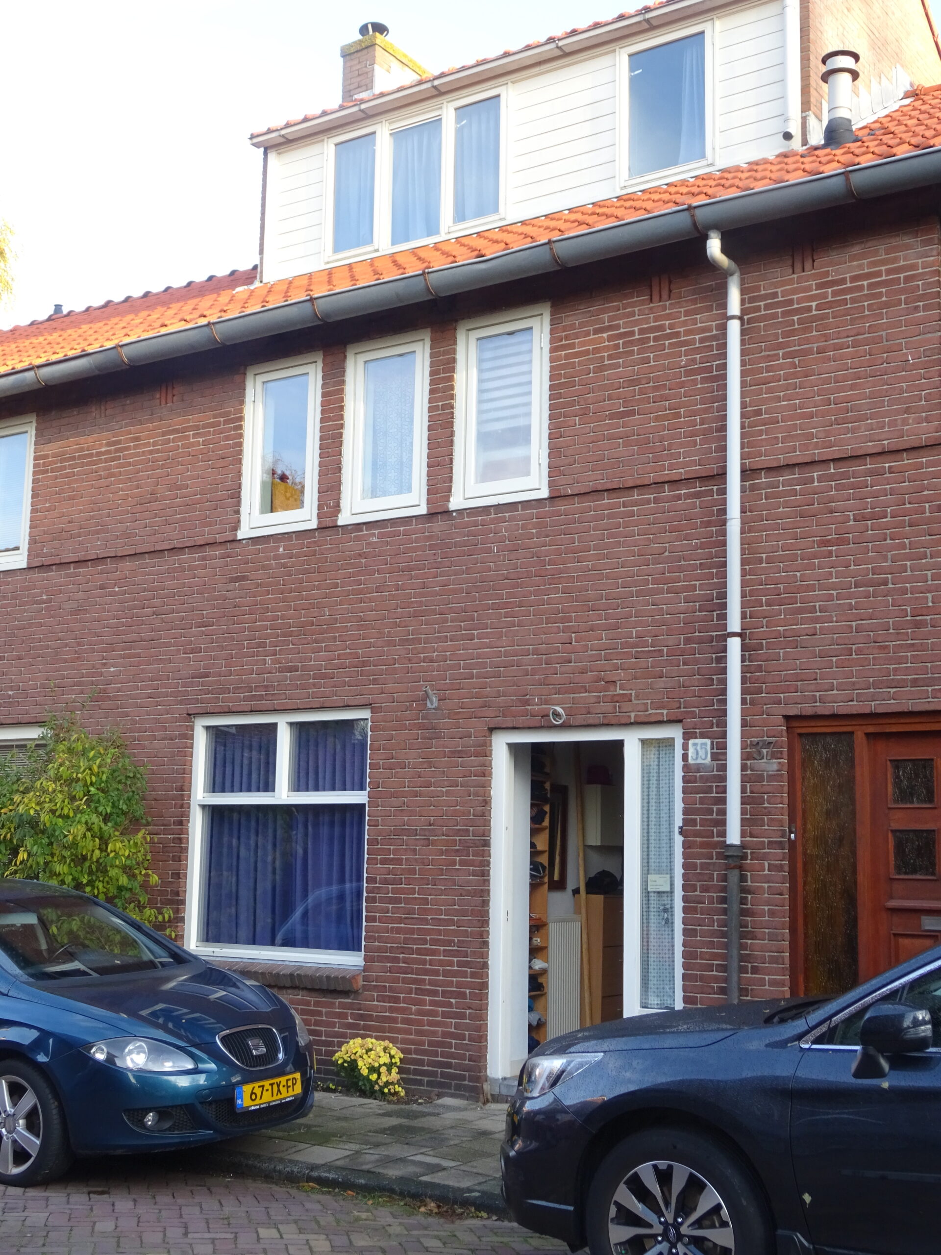 Bakstenen rijwoning in het Ramplaankwartier met dakkapel en geparkeerde auto's voor de deur.