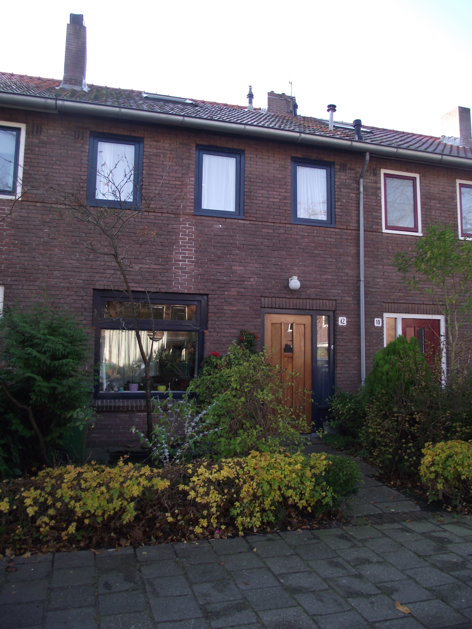 Bakstenen rijwoning in het Ramplaankwartier met donkere kozijnen en een voortuin.