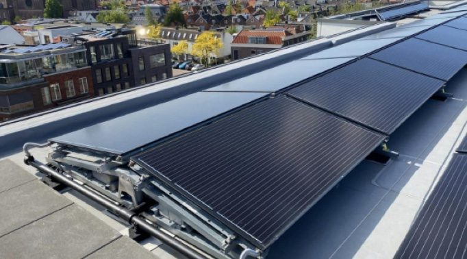 Zwarte zonnepanelen schuin op een montagesysteem op een plat dak, in rijen met ruimte ertussen.