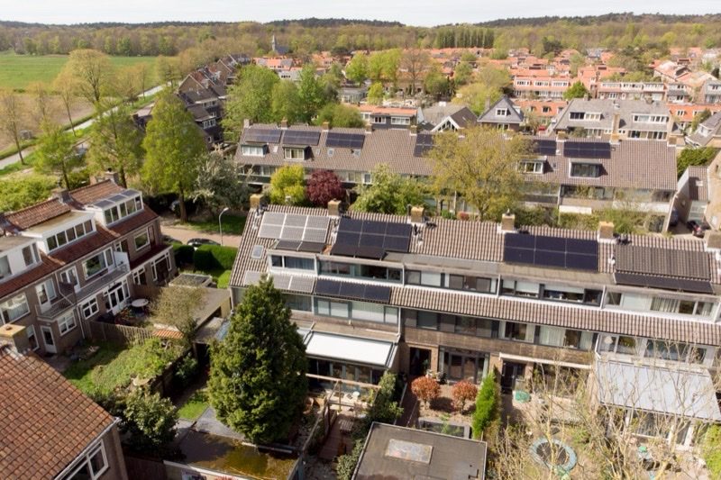 Luchtfoto van het Ramplaankwartier: rijtjeswoningen waarvan de pannendaken vlak in het dakvlak zijn belegd met zonnepanelen, verdeeld over meerdere dakvlakken.