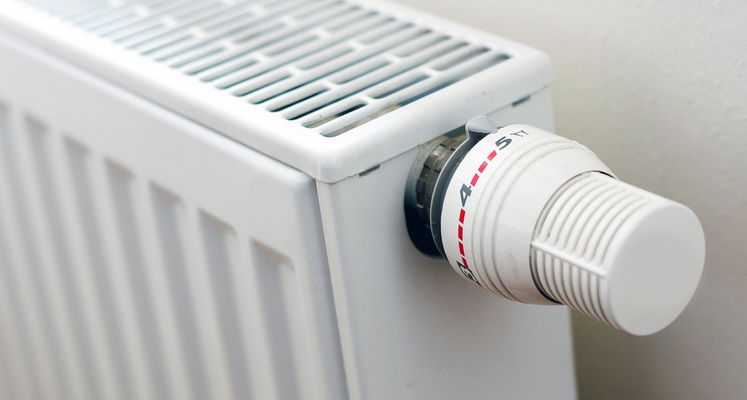 Close-up van een witte paneelradiator met een thermostaatkraan aan de zijkant.